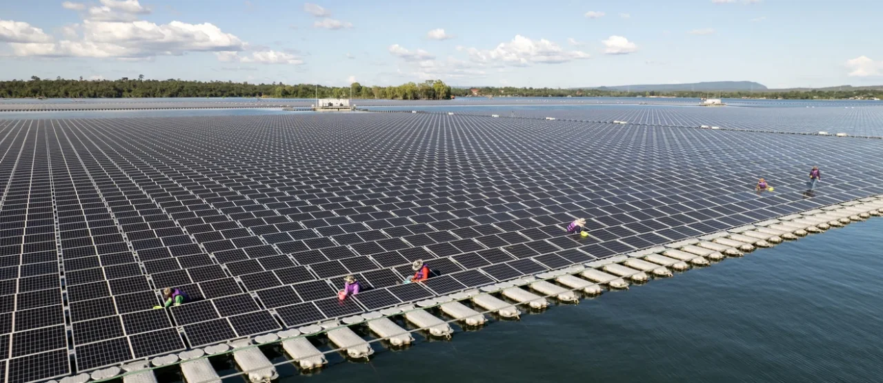 High-quality editorial photography for Thai technology blog, Floating solar array on a Thai reservoir water surface, educational demonstration of alternative installation, tropical environment with mountains in background, peaceful innovation atmosphere, bright daylight, brand-neutral educational focus